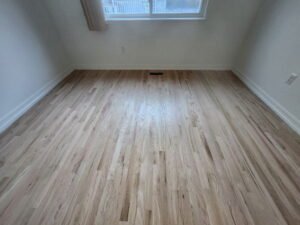 Freshly sanded and finished red oak hardwood flooring in an empty bedroom with white baseboards.