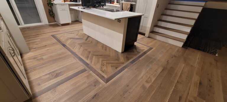 White oak kitchen floor with straight floor meeting a border with herringbone next to island.